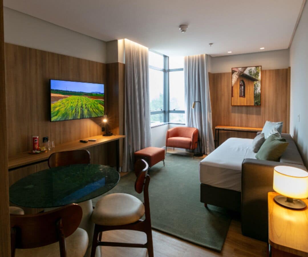 A modern hotel room with a large TV, a dining table, a sofa, and a bed.