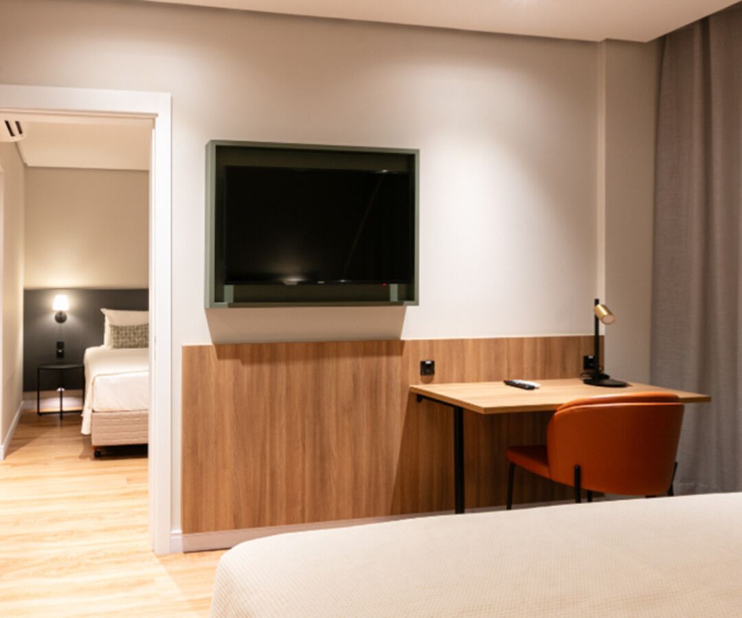 Une chambre d’hôtel comprenant un lit, un bureau avec une chaise, un téléviseur fixé au mur et une table de chevet avec une lampe.