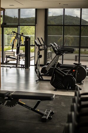Un gimnasio con equipo de ejercicio, ventanas amplias y vistas a zonas verdes.