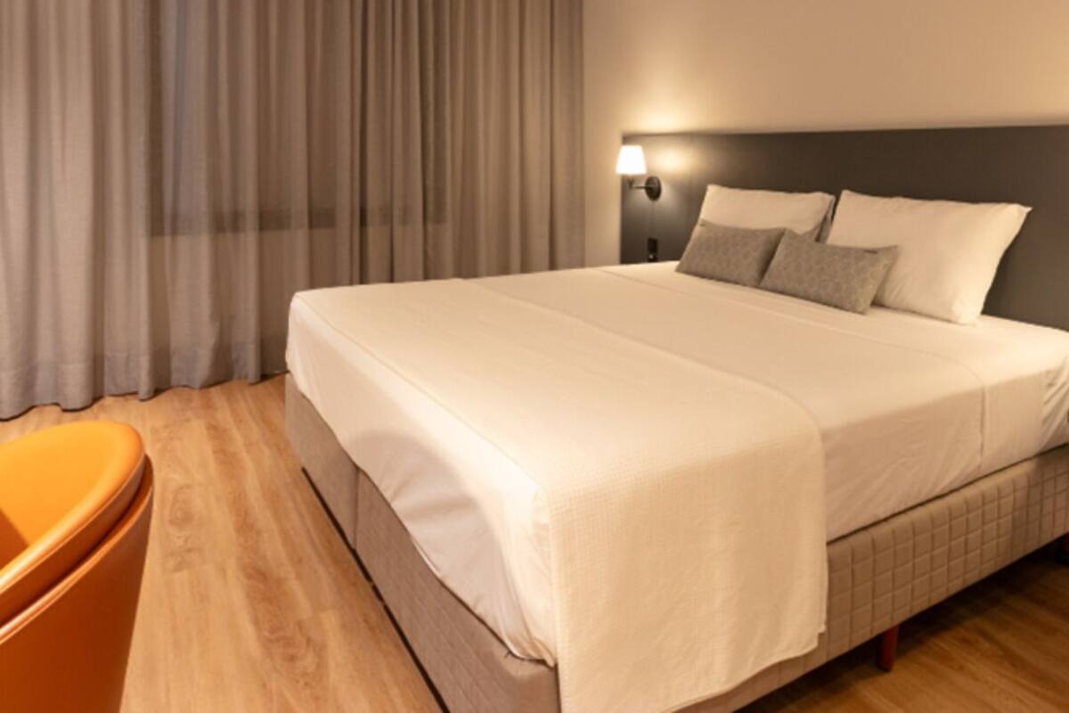 Una cama bien hecha con cabecera, una lámpara de noche y una silla.