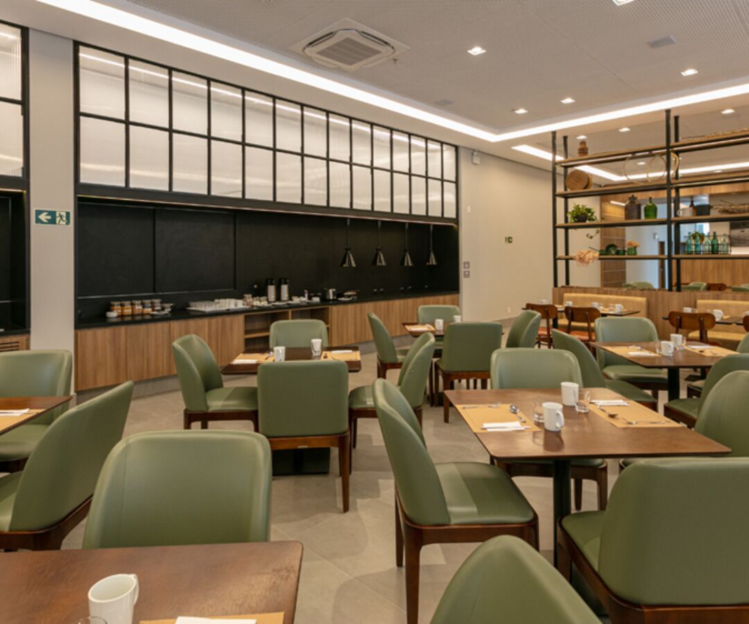 Un restaurant moderne avec des chaises et des tables vertes, un mur noir ardoise et une étagère remplie de bouteilles et de bocaux.
