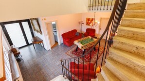 Un vaste espace de vie comprenant un canapé rouge, une table de baby-foot et un escalier.