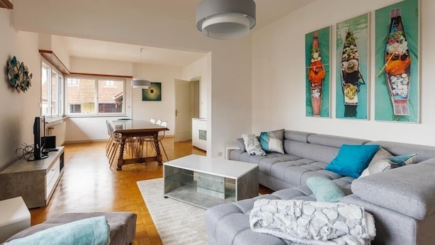 Un salon moderne avec un canapé gris, une table basse et un coin repas comprenant une table et des chaises en bois.
