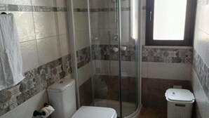 A bathroom with a glass-enclosed shower, a toilet, and a trash bin.