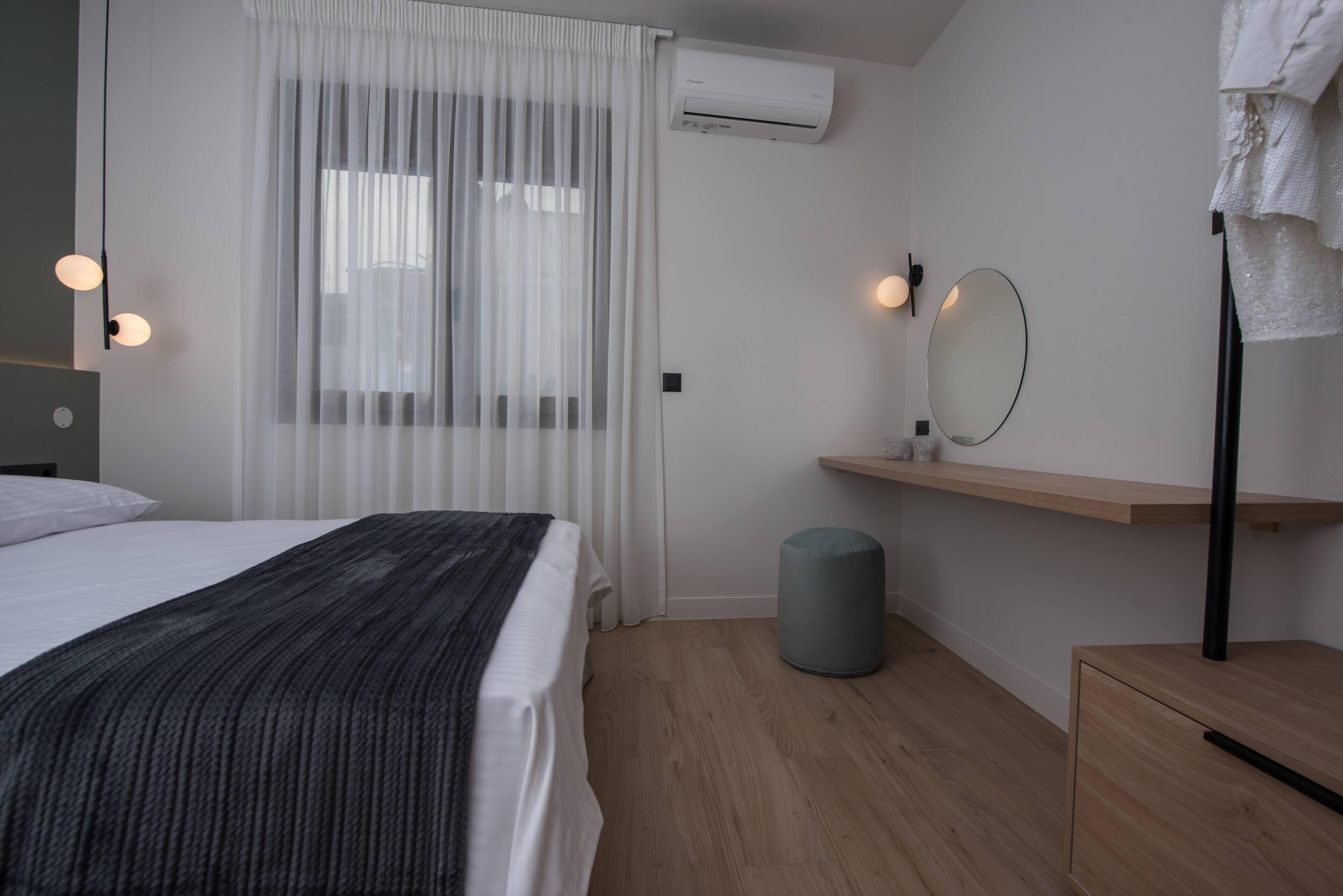 Et moderne soveværelse med seng, natbord, spejl, en lille skammel og en vægmonteret aircondition.