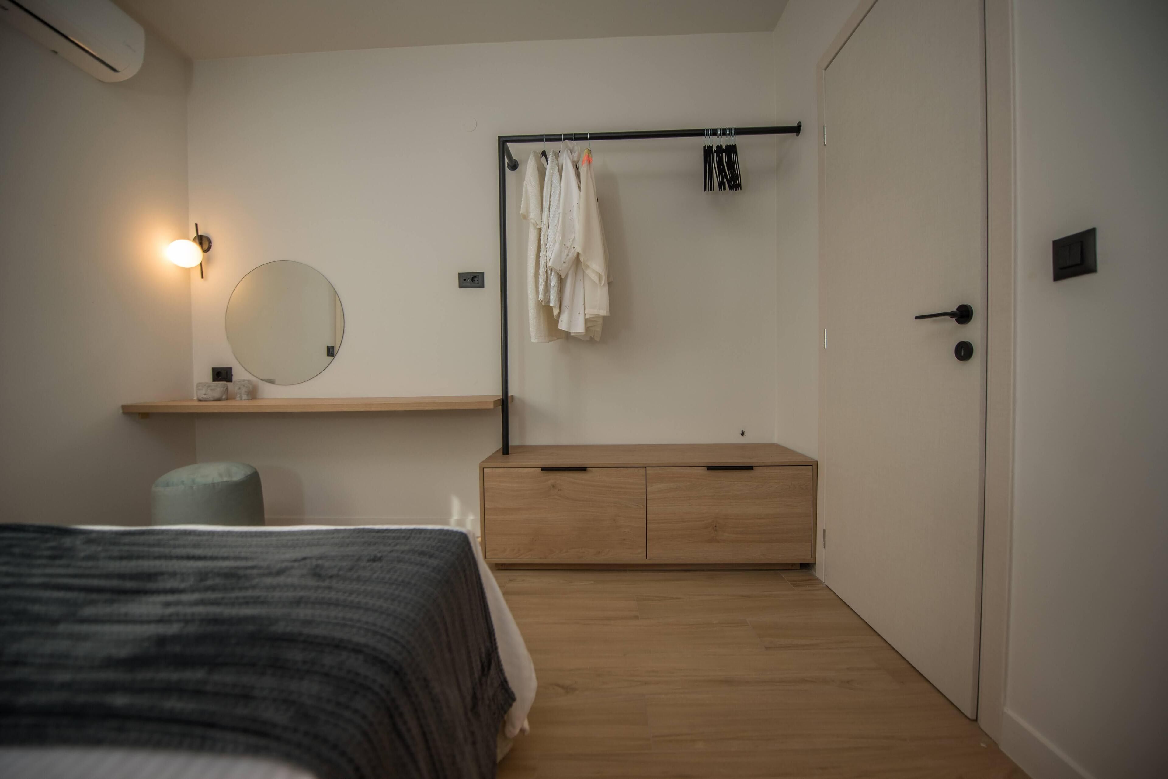 A bedroom with a bed, a bedside table, a mirror, a wardrobe, and a hanging clothes rack.