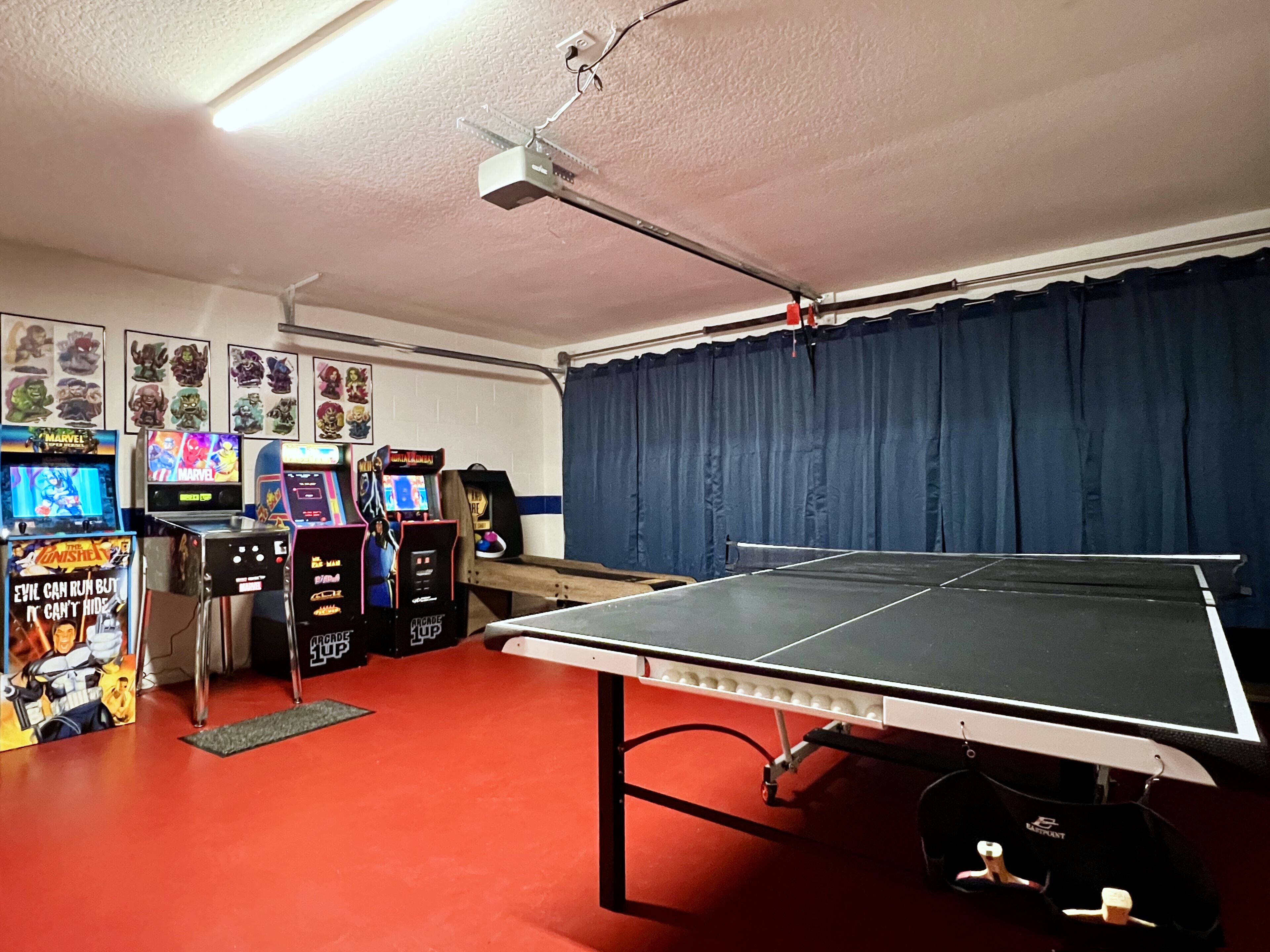 A room with a ping pong table, arcade games, and a ceiling-mounted projector.