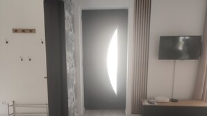 Un soggiorno moderno con pavimento in legno, una TV su un mobile e una grande finestra che si affaccia all'esterno.