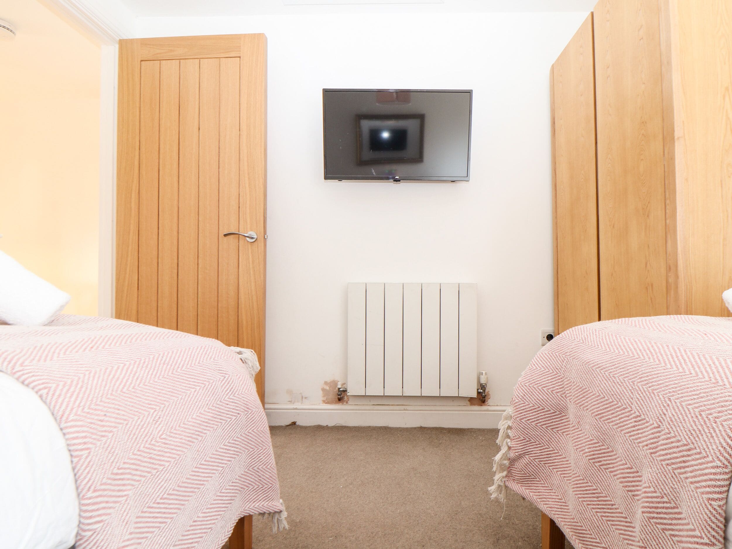 A bedroom with two beds, a wooden wardrobe, a mounted TV, and a radiator.