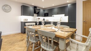 Une cuisine moderne avec des meubles de couleur sombre, un plan de travail blanc et une table à manger en bois pour quatre personnes.