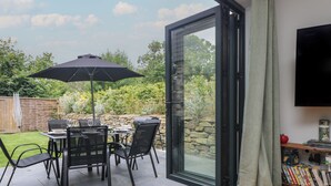 Une terrasse avec une table et des chaises, un barbecue et un téléviseur dans une pièce.