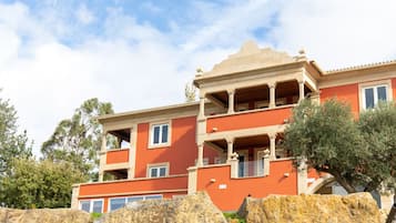 A multi-story building with balconies, large rocks in the foreground, and trees in the background.