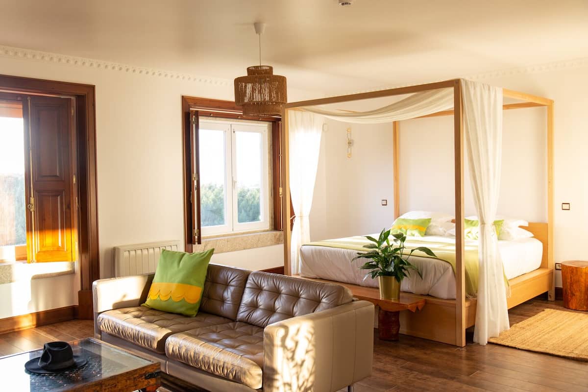 A bedroom with a four-poster bed, a leather sofa, a coffee table, and a large window.