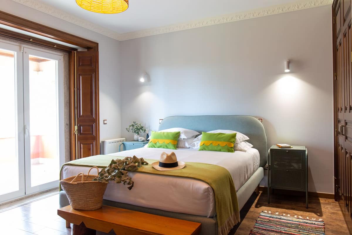 A bedroom with a bed, bedside tables, a lamp, a basket, and a suitcase.