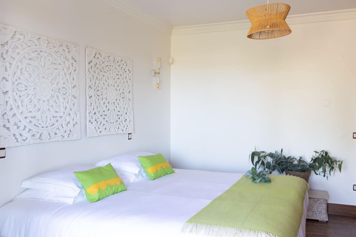 A bedroom with a large bed, two decorative wall panels, a hanging light fixture, and a potted plant.