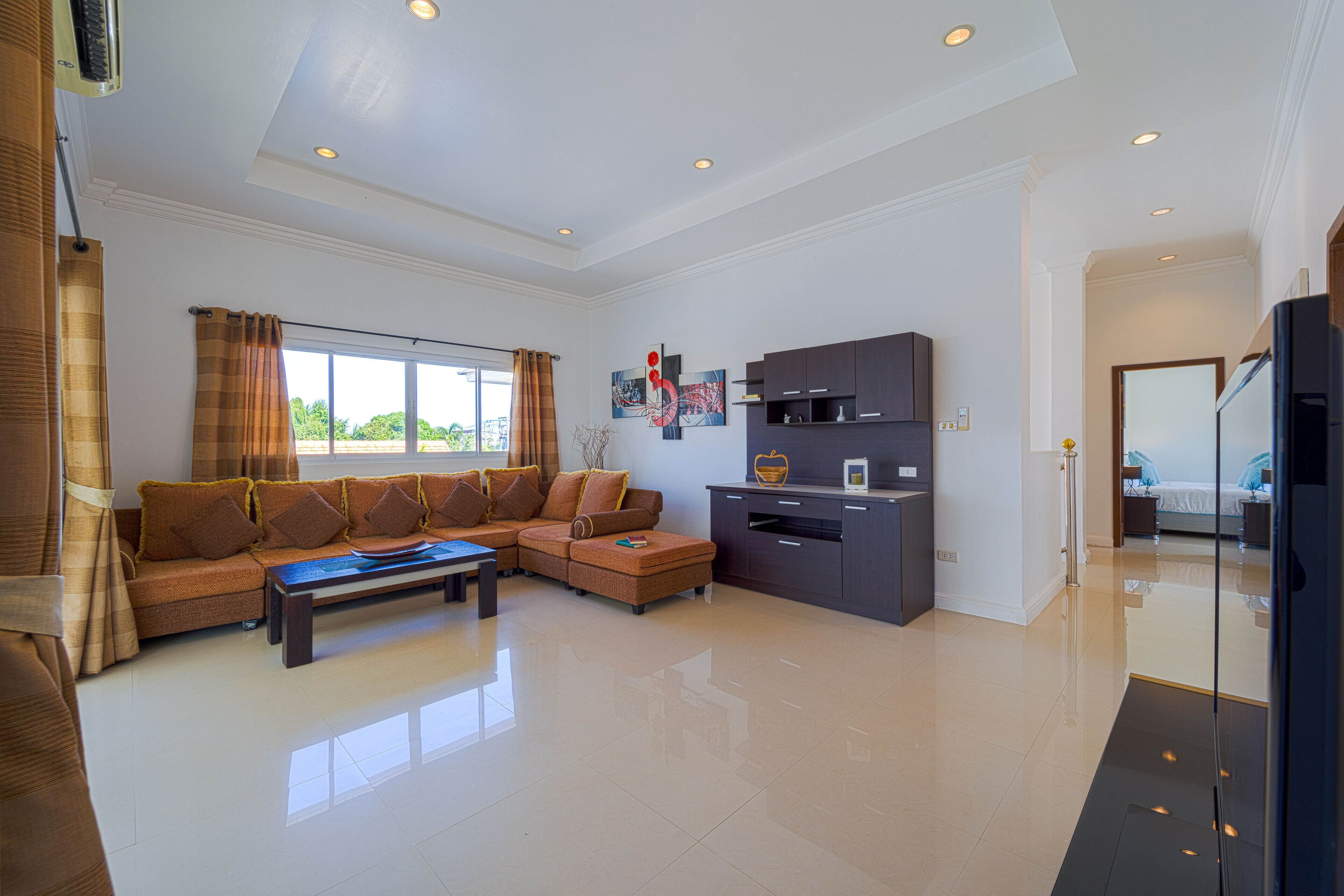 A modern living room with a sectional sofa, a coffee table, and a kitchen area with dark cabinets and a countertop.