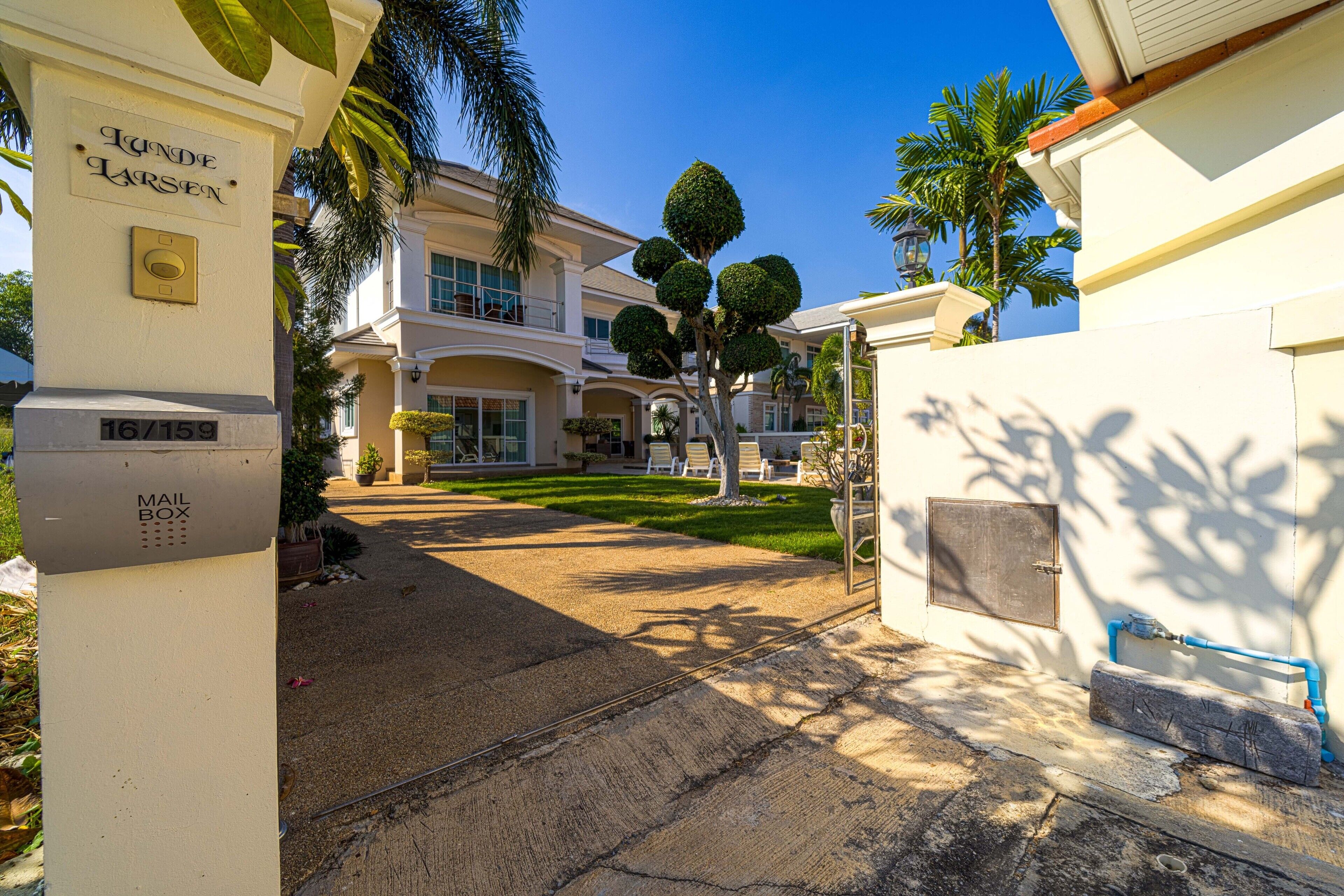 A gated entrance with a mailbox, a well-maintained lawn, and a large building with multiple balconies.