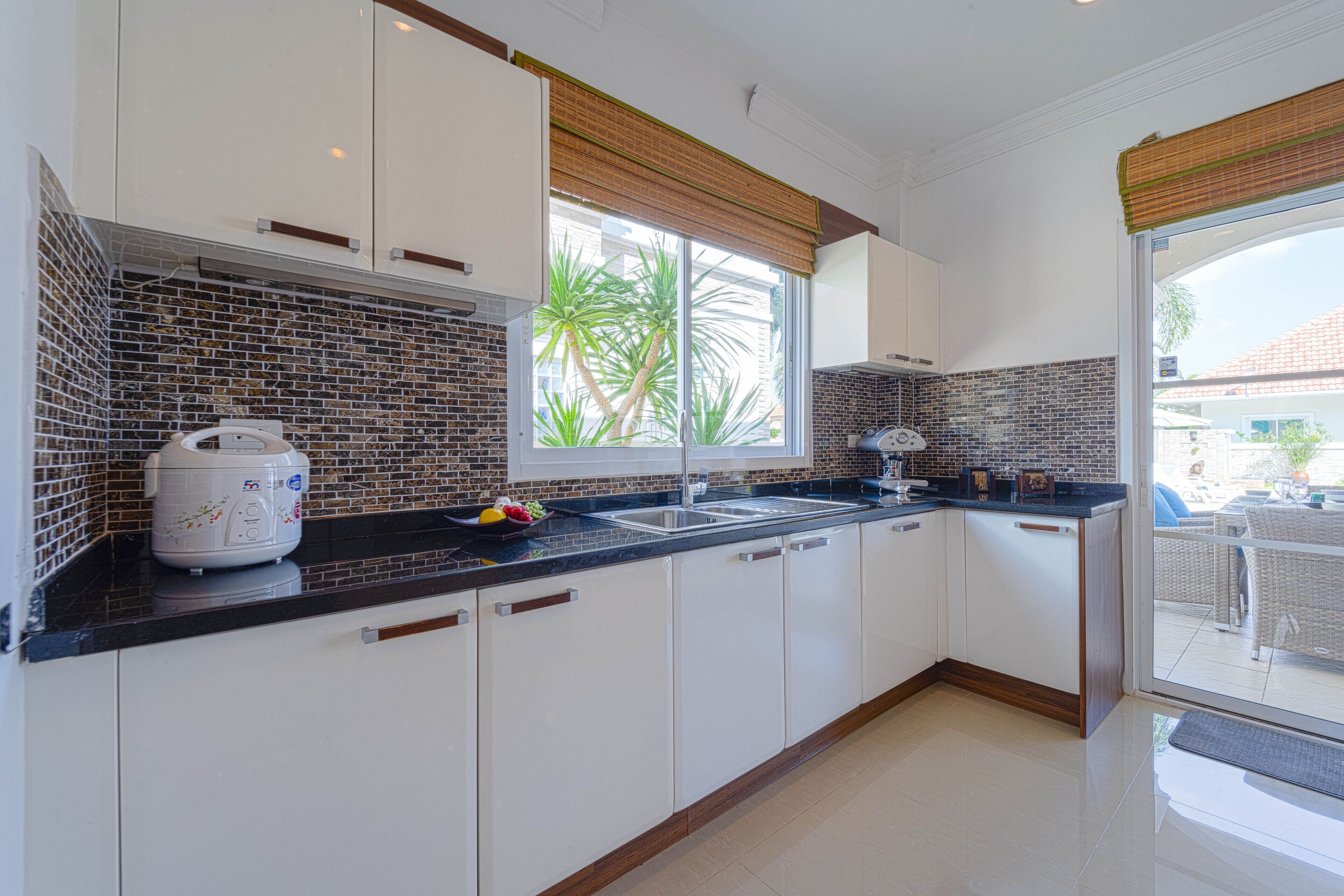 A modern kitchen with white cabinets, a black countertop, and a window with a view of palm trees.