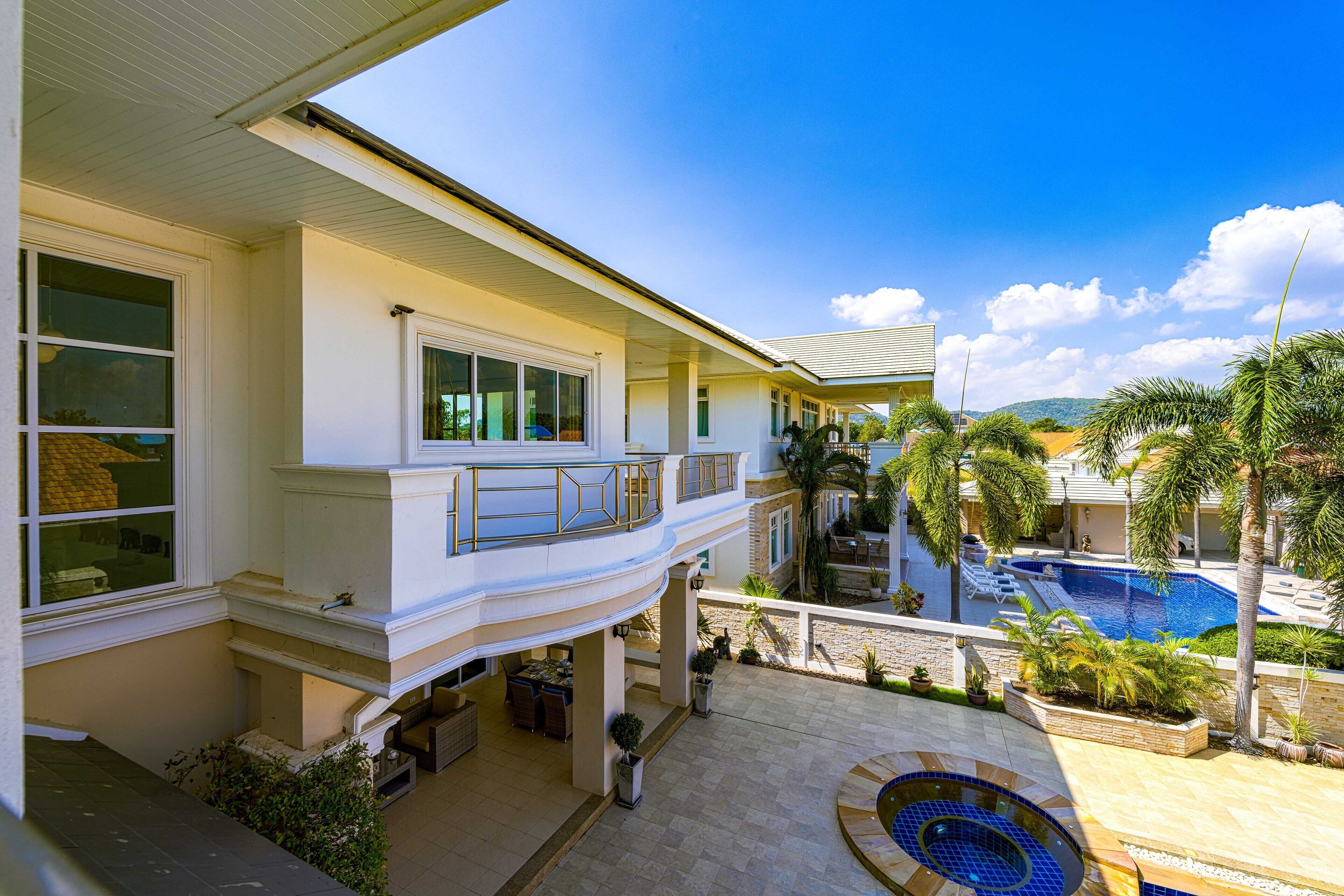 Ein zweistöckiges Haus mit Balkon mit Blick auf einen Pool und einen angelegten Garten.