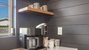 Une cuisine équipée d’une machine à café, d’une cafetière et d’une étagère où sont rangées des tasses.