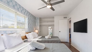 Habitación de hotel con dos camas, ventilador de techo, televisión y ventana con persianas.