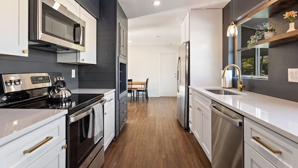 Una cocina moderna con electrodomésticos de acero inoxidable, piso de madera y un comedor con mesa y sillas.