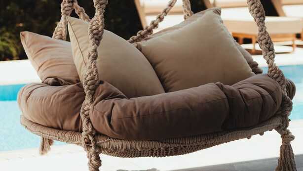 Silla colgante de cuerda con cojines junto a una piscina.