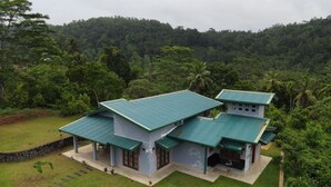 A two-story house with a green roof, surrounded by lush greenery and a stone wall. - Be with nature and Mountain view (Matara)