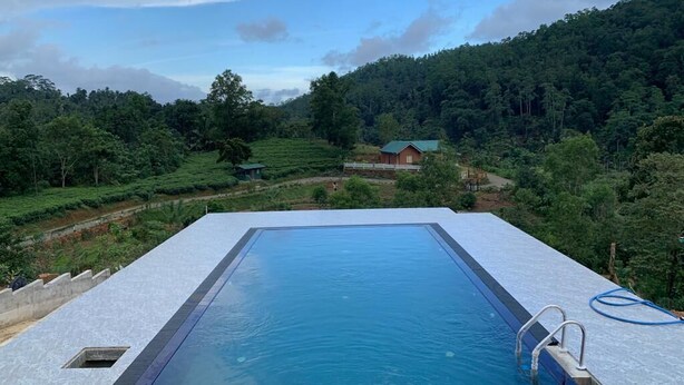 A rectangular pool with a clear blue water surface, surrounded by a white deck. In the background, there is a green-roofed building amidst a lush, green landscape with terraced fields. - Be with nature and Mountain view (Matara)