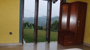 A room with a large bed, a wooden wardrobe, and a sliding glass door leading to a grassy outdoor area. - Be with nature and Mountain view (Matara)