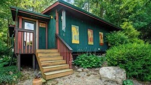 A cabin with a wooden staircase leading to a door, surrounded by greenery and rocks. - Beautiful Oasis | Sauna | Mohican Getaway (Perrysville)