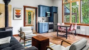 A modern living room with a fireplace, a dining area with pink chairs, and a kitchen with blue cabinets. - Beautiful Oasis | Sauna | Mohican Getaway (Perrysville)