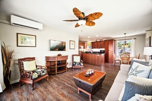 Uma sala de estar espaçosa com um ventilador de teto de madeira, uma área de cozinha com armários de madeira e um espaço de jantar com móveis de vime.