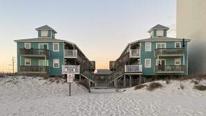 Een strandpand met twee verdiepingen, een houten trap en een bord met daarop 'Sunrise Village 1159 West Beach Blvd.'.
