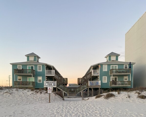 Une propriété située en bord de mer, avec des bâtiments à deux étages, un escalier en bois et une enseigne indiquant « Sunrise Village, 1159, boulevard West Beach ».