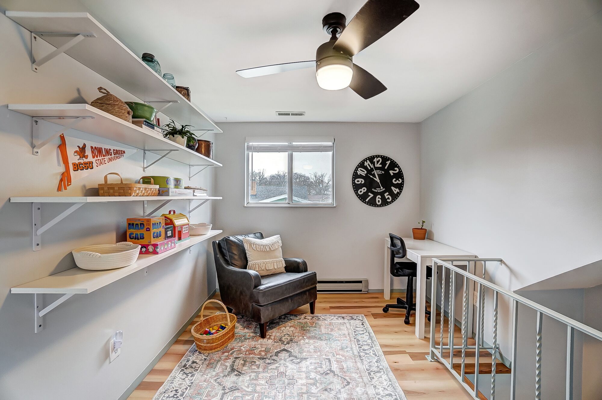 A modern living room with white shelves, a black leather sofa, a patterned rug, and a large wall clock.