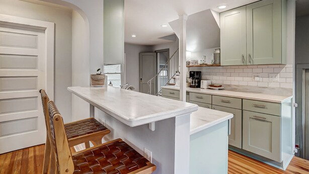 Una cocina con encimera de mármol, taburetes de madera y armarios verde claro.