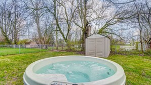 Un jacuzzi en un patio trasero, con un cobertizo y árboles al fondo.