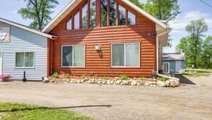 Une cabane en rondins avec un toit à pignon, deux grandes fenêtres et un petit porche.