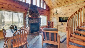 L’intérieur chaleureux d’un chalet avec une cheminée en pierre, des meubles en bois et un téléviseur fixé au mur.