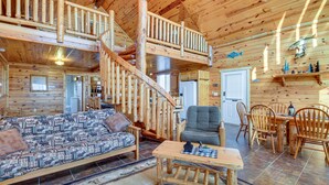Une cabine spacieuse avec un plafond haut, un escalier en bois, un coin repas avec une table et des chaises, et un canapé agrémenté de coussins à motifs.