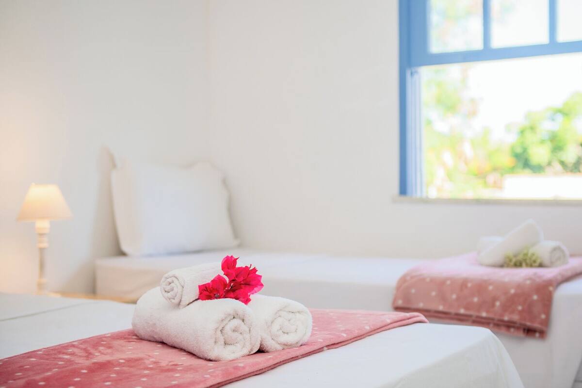 A hotel room with two beds, each with a rolled towel and a pink polka-dotted blanket.