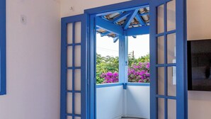 A room with a bed, a pair of rolled towels, and an open blue door leading to a balcony with pink flowers. - Pousada Vila Capri (Búzios)