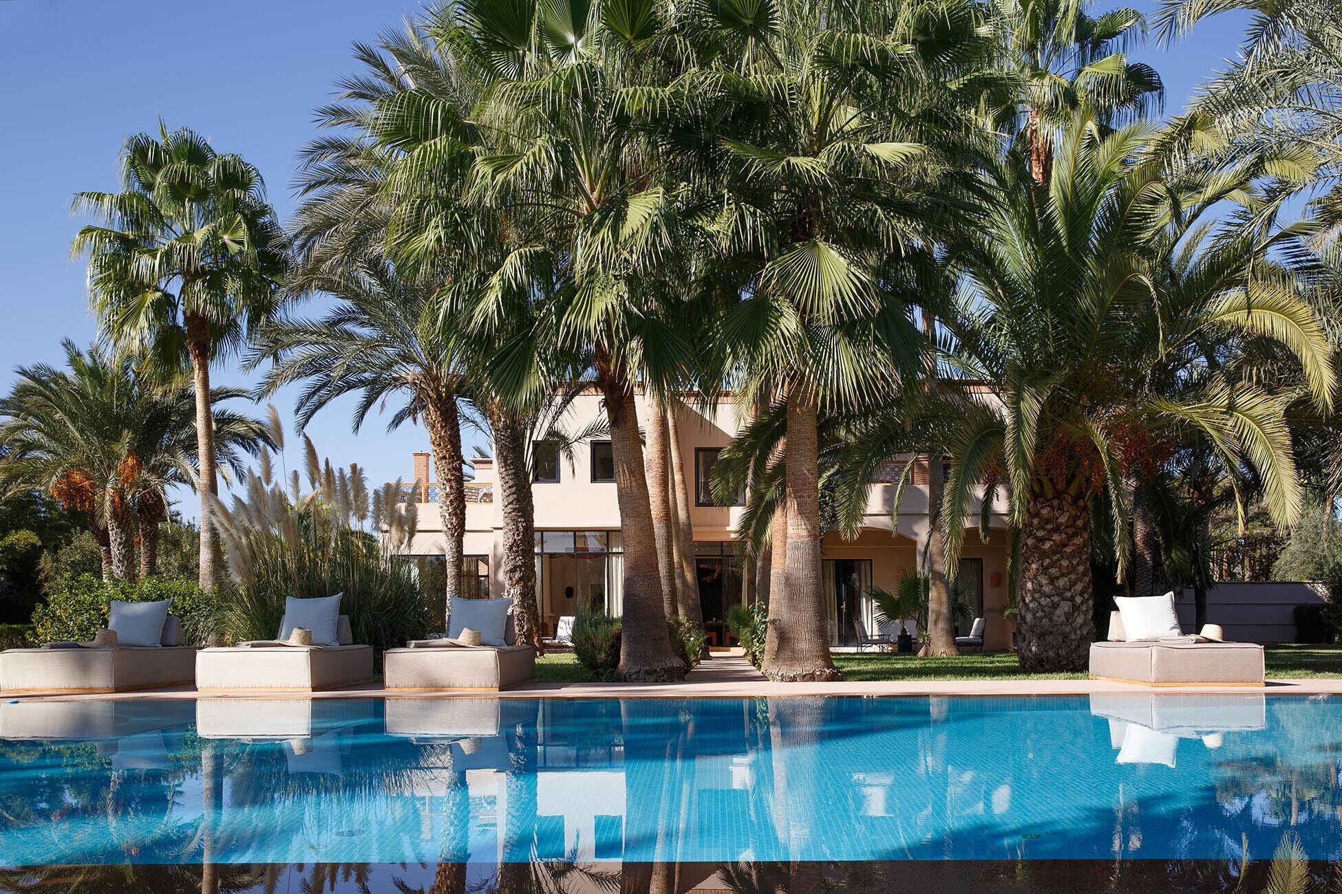 A poolside area with a clear blue pool, palm trees, and a building with multiple balconies.