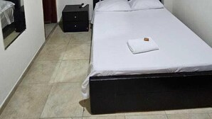 A bedroom with a bed, an air conditioning unit, a nightstand, a suitcase, and a painting on the wall. - Hotel Barranquilla Inn (Barranquilla)