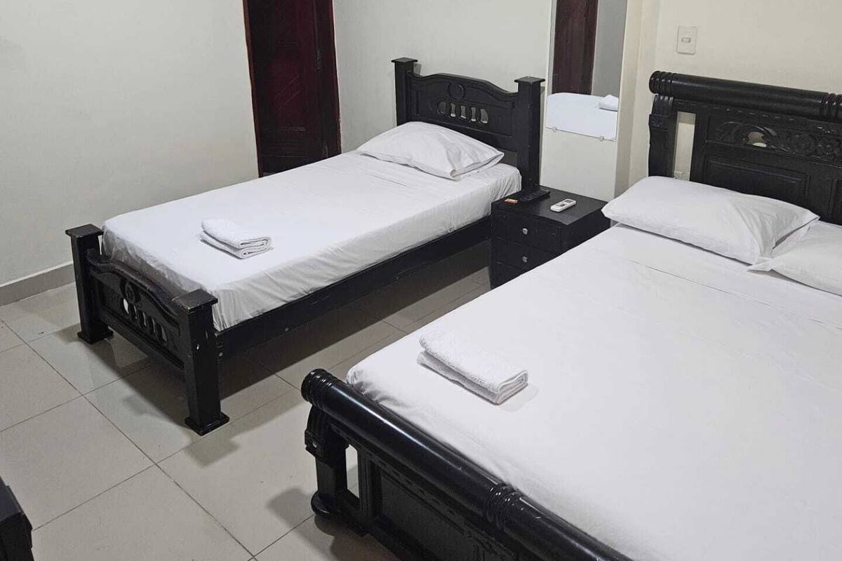 A hotel room with two single beds, a dark wooden headboard, a small bedside table, and a mirror on the wall.
