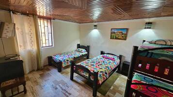 Une chambre avec deux lits simples, un plafond en bois, une fenêtre avec des rideaux, un tableau au mur et un bureau avec une chaise.