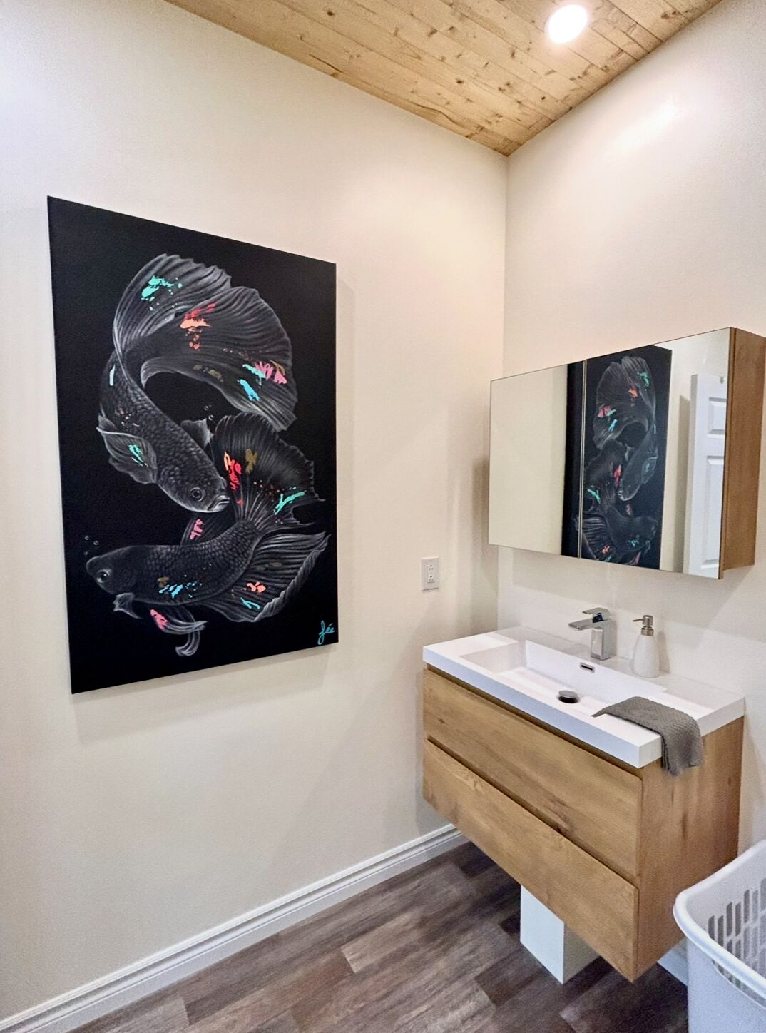 A modern bathroom with a large abstract painting, a white sink, and a wooden vanity.