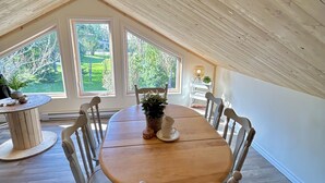Un'area pranzo con un tavolo e sedie in legno, ampie finestre che si affacciano sull'esterno e un soffitto con travi a vista.