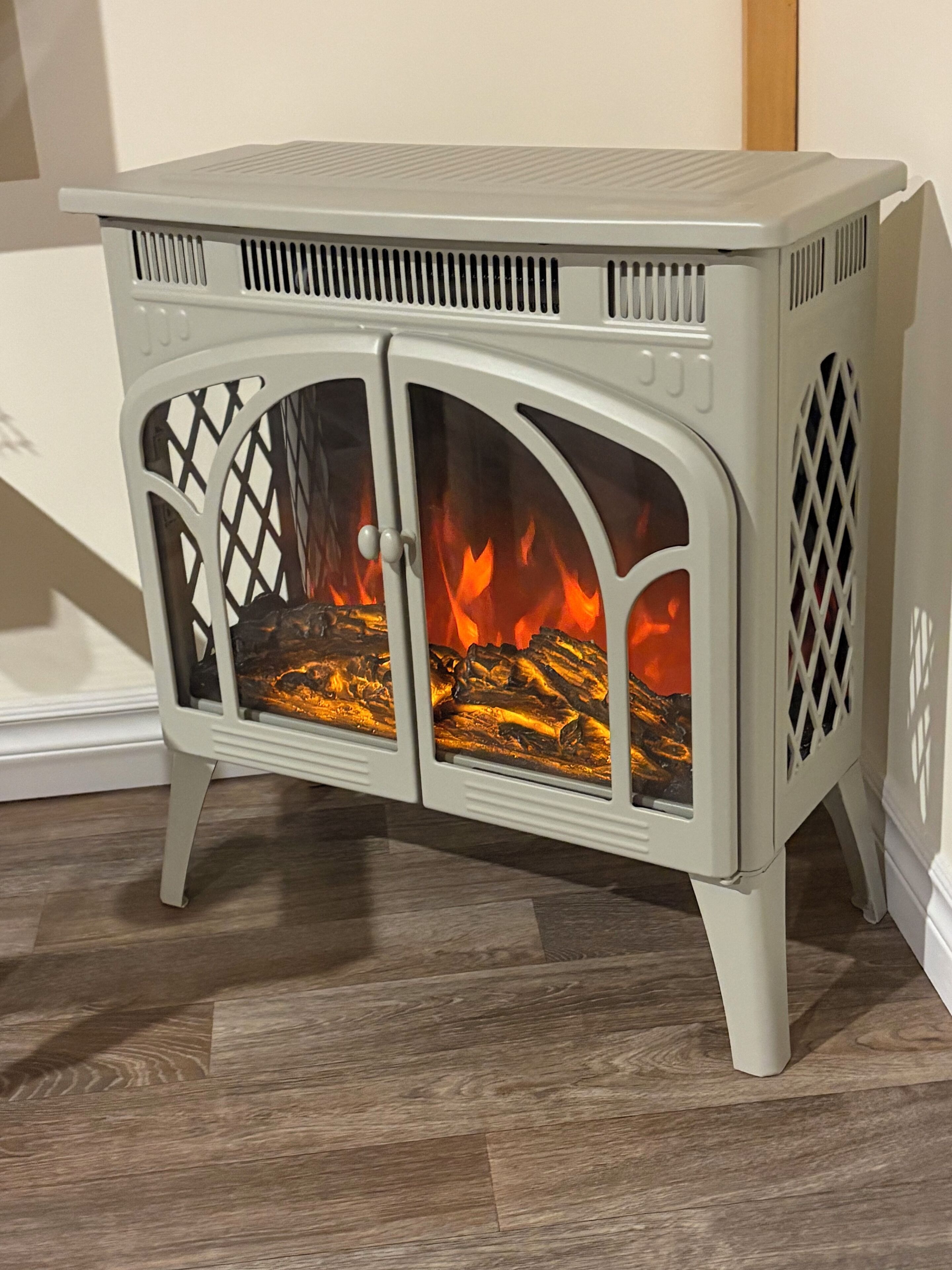 Un poêle à bois blanc, doté de portes en verre, à travers lesquelles on peut voir le feu qui brûle à l’intérieur.